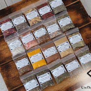 May include: A wooden box filled with small clear plastic bags containing various dried herbs and spices. Each bag has a label with the name of the herb or spice and a description of its uses. The box is labeled "The Norse Wind".