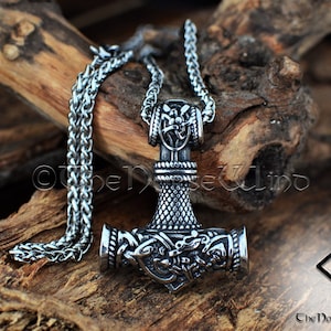 May include: Silver Mjolnir pendant necklace with intricate knotwork and a braided chain. The pendant features a detailed design of the hammer of Thor, a symbol of strength and protection in Norse mythology.