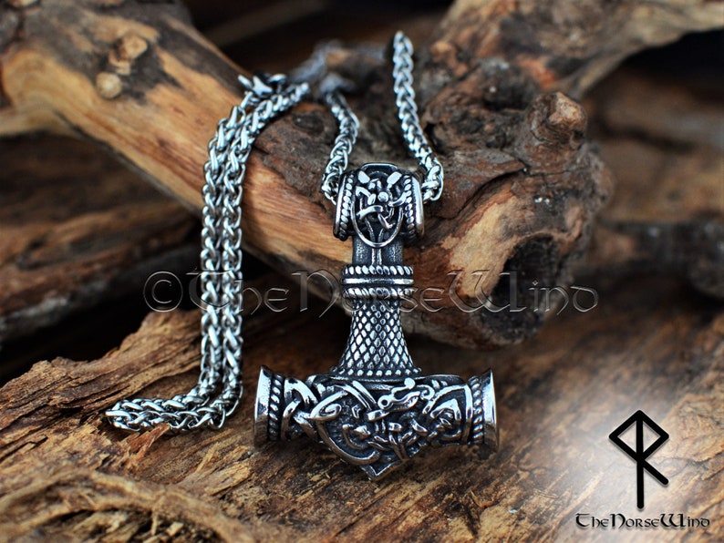 May include: Silver Mjolnir pendant necklace with intricate knotwork and a braided chain. The pendant features a detailed design of the hammer of Thor, a symbol of strength and protection in Norse mythology.