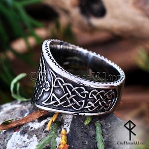 May include: A silver ring with a Celtic knot design and a bird motif. The ring is made of stainless steel and has a textured finish.