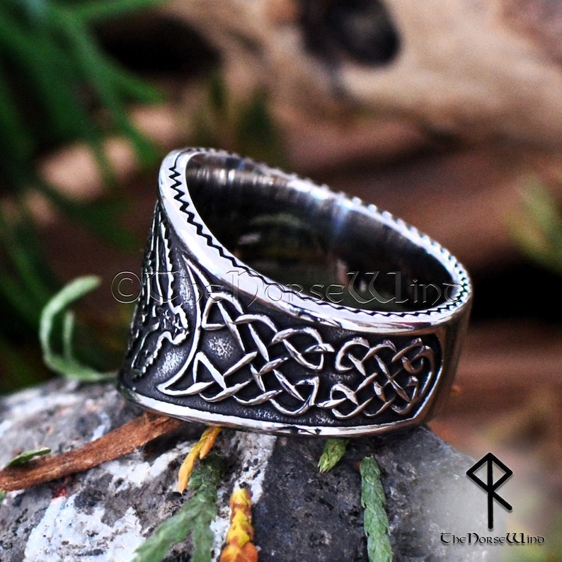 May include: A silver ring with a Celtic knot design and a bird motif. The ring is made of stainless steel and has a textured finish.