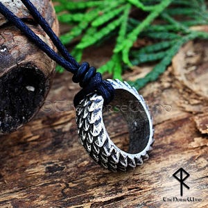 Peut inclure: Un collier avec un pendentif en argent de forme circulaire orné d'un motif texturé en forme d'écailles. Le pendentif est attaché à un cordon noir.