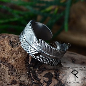 May include: A silver adjustable ring featuring a detailed feather design. The ring is crafted from stainless steel and has a textured finish.