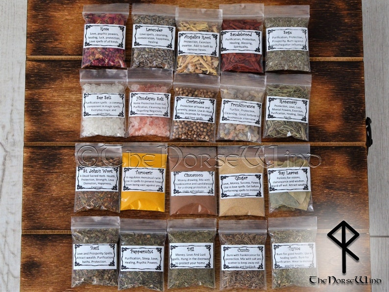 May include: A collection of 20 small clear plastic bags filled with various herbs and spices. Each bag has a white label with the name of the herb or spice and its associated magical properties. The bags are arranged in four rows of five on a wooden surface. The labels include names like Rose, Lavender, Augalic Root, Sandalwood, Sage, Sea Salt, Himalayan Salt, Coriander, Fresh Orange, Rosemary, St. John's Wort, Turmeric, Cinnamon, Ginger, Bay Laurel, Yarrow, Peppermint, Money & Luck, Oregano, and Thyme.
