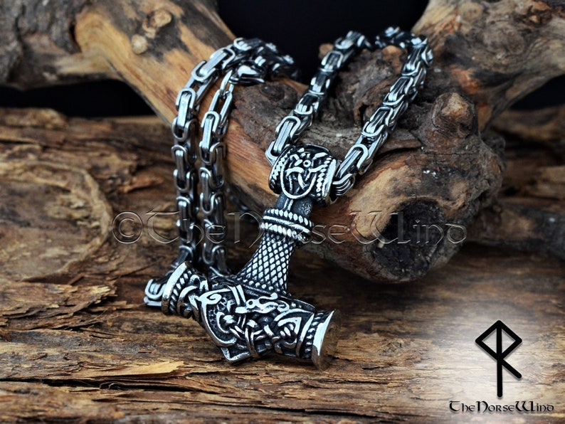 May include: A silver Mjolnir pendant necklace with intricate details and a braided chain. The pendant features a detailed design of the hammer head with a dragon head on the side. The chain is a box chain with a secure clasp.