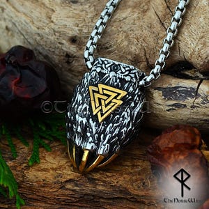 Könnte beinhalten: Eine Halskette mit einem silbernen und goldenen Anhänger, der einen Wolfskopf mit einem goldenen Valknut-Symbol zeigt. Der Anhänger ist an einer silbernen Kette.