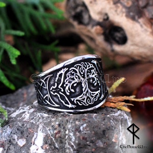 May include: A silver ring with a detailed design of a tree of life. The ring is wide and has a curved shape.