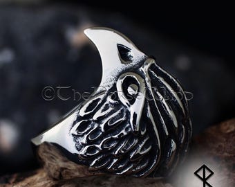 May include: A silver ring featuring an intricate design of a bird's head with its beak open. The ring is crafted from stainless steel and has a textured finish.