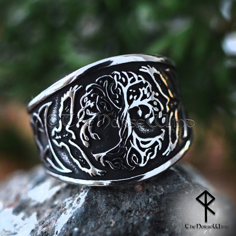 May include: A silver ring with a detailed design of a tree with intricate branches and leaves. The ring is wide and has a polished finish.