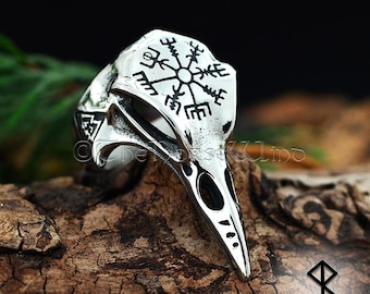 May include: A silver ring with a raven skull design and a Vegvisir compass symbol. The ring is made of stainless steel and has a black finish.