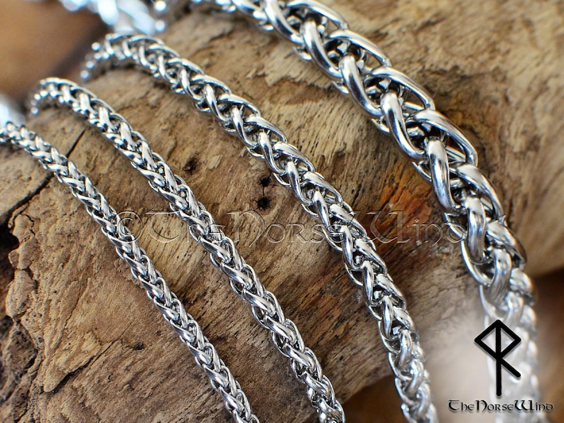 May include: Four silver braided chains of different widths, lying on a wooden surface. The chains are interlocked and appear to be made of metal.