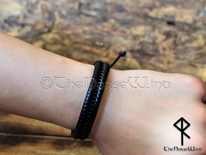 May include: A black leather bracelet with a braided design. The bracelet is tied with a knot and is worn on a person's wrist.
