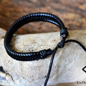 May include: Black leather bracelet with a braided design and a simple knot closure. The bracelet is adjustable and has a black cord.