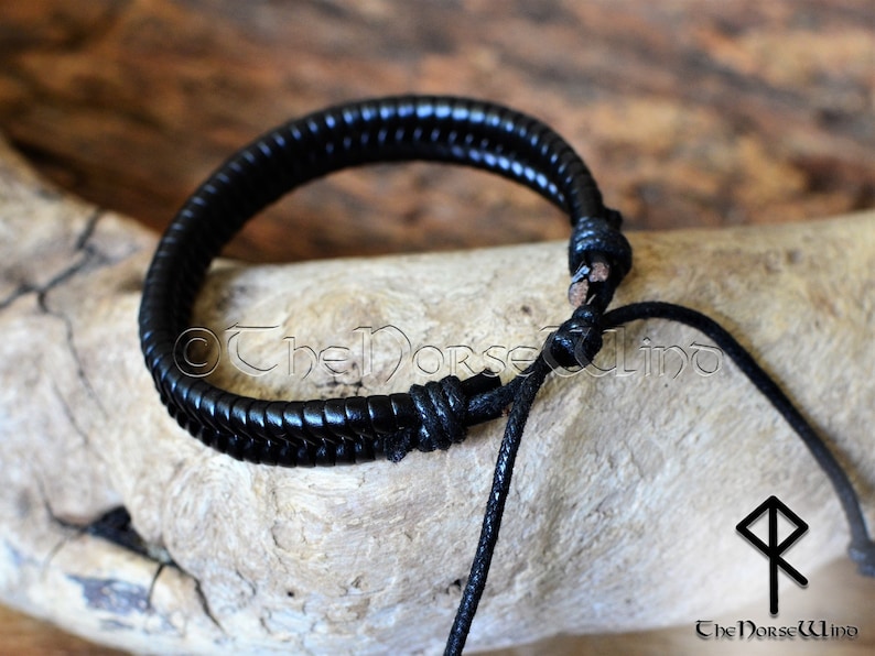 May include: Black leather bracelet with a braided design and a simple knot closure. The bracelet is adjustable and has a black cord.