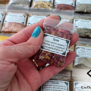 May include: A small clear plastic bag filled with dried rose petals. The bag has a white label with the text "Rose Love, psychic powers, healing, luck, protection. Love spells of all kinds."