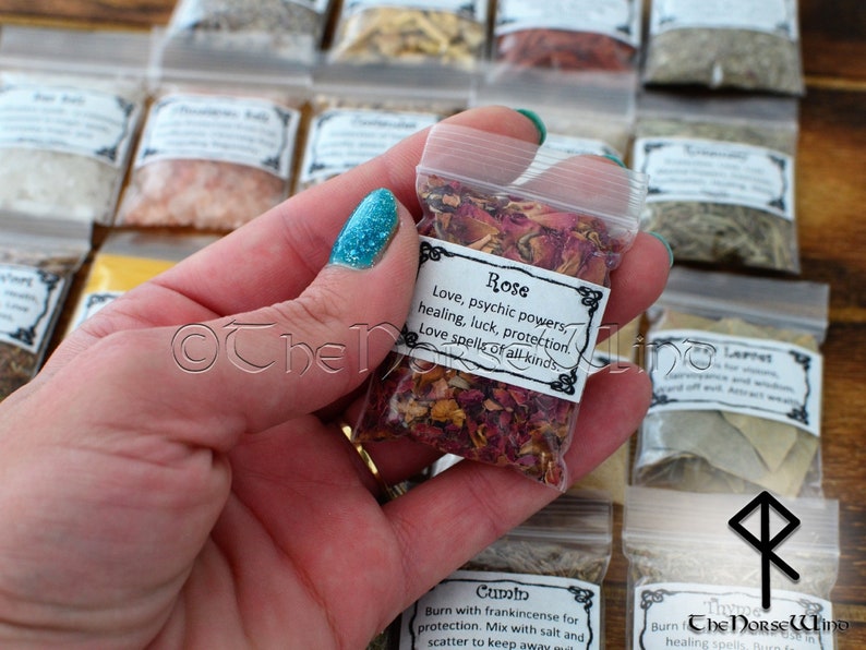 May include: A small clear plastic bag filled with dried rose petals. The bag has a white label with the text "Rose Love, psychic powers, healing, luck, protection. Love spells of all kinds."