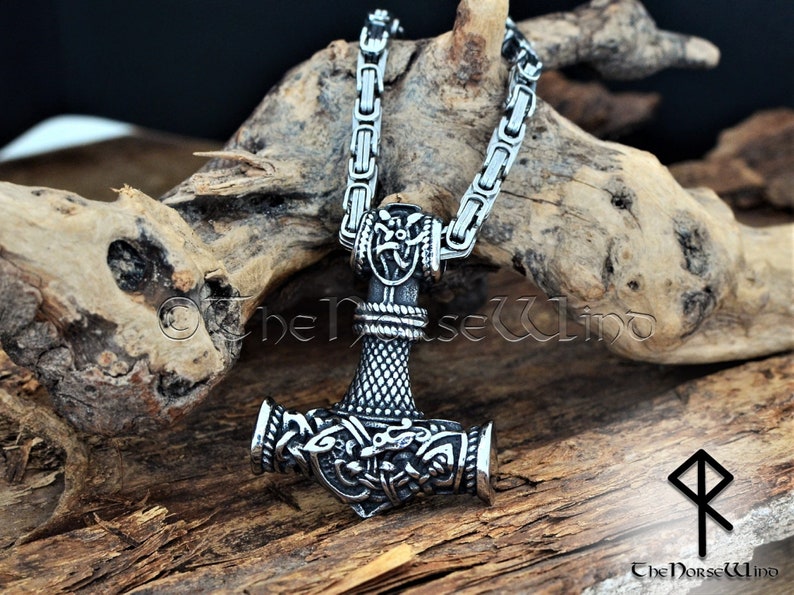 May include: A silver Mjolnir pendant necklace with intricate details and a braided chain. The pendant features a detailed design of the hammer head with a knotwork pattern and a wolf's head on each side. The chain is a box chain with a secure clasp.