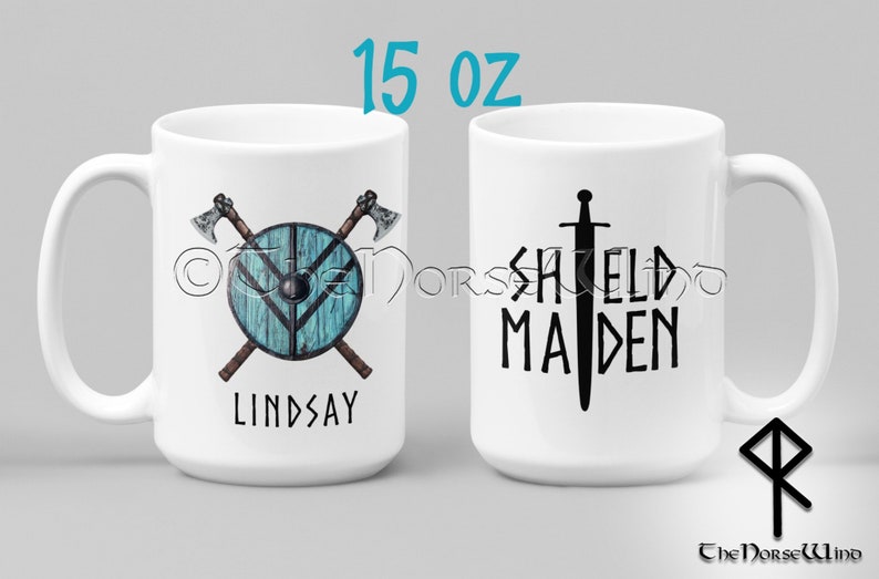May include: White ceramic mug with a 15 oz capacity. One side features a shield with crossed axes and the name "LINDSAY". The other side features a sword and the text "SHIELD MAIDEN".