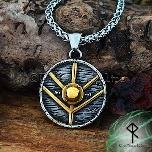 Op de afbeelding: Een zilveren en gouden ketting met een hanger in de vorm van een rond schild met een gestileerd boomontwerp en een centrale boss. Het schild is gedetailleerd met een getextureerd oppervlak en een gevlochten ketting.