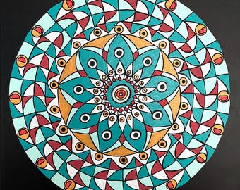 Puede incluir: Un mandala de color turquesa, dorado, blanco y rojo con un patrón geométrico. El mandala está pintado sobre un fondo negro.