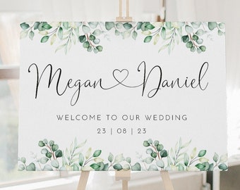 Peut inclure: Une pancarte de bienvenue de mariage avec un fond blanc et un feuillage aquarelle vert. La pancarte indique "Megan & Daniel" avec un symbole de cœur entre les noms. Le texte ci-dessous indique "Bienvenue à notre mariage" et la date "23 | 08 | 23".