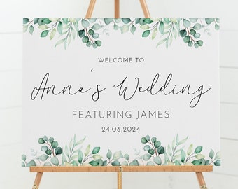 Peut inclure: Une pancarte d'accueil blanche avec des feuilles vertes en aquarelle et le texte "Bienvenue au mariage d'Anna avec James 24.06.2024" affichée sur un chevalet en bois.