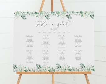 Peut inclure: Un plan de table de mariage blanc avec un feuillage vert et le texte "Take a seat" en haut. Le plan liste les noms des invités par numéro de table.