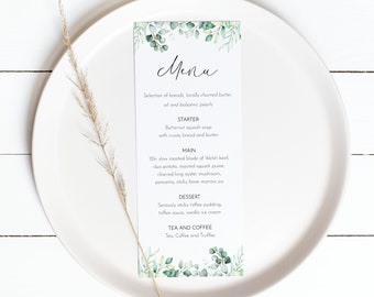 Peut inclure: Une assiette blanche avec une carte de menu dessus. La carte de menu a un motif de feuilles vertes et le texte "Menu" en écriture cursive noire. Le menu liste une sélection de pains, du beurre baratté localement et des poires anciennes, suivi d'un apéritif, d'un plat principal, d'un dessert et d'options de thé et de café.