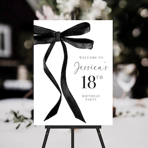 May include: A white sign featuring a black bow illustration and the text "WELCOME TO Jessica's 18th BIRTHDAY PARTY." The sign is displayed on a black easel, ideal for an eighteenth birthday celebration.