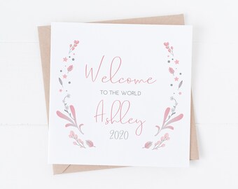 May include: A white card with a pink floral wreath border. The text reads "Welcome to the world Ashley 2020".