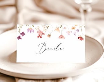 Puede incluir: Una tarjeta de lugar blanca con un diseño floral en tonos de rosa, morado y naranja. El texto "Bride" está escrito en caligrafía negra.