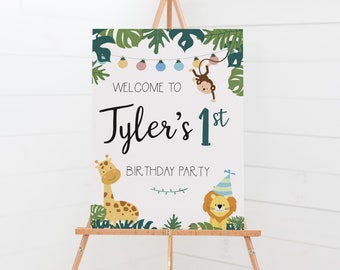 May include: Welcome to Tyler's 1st Birthday Party sign with a jungle theme. The sign features a monkey hanging from vines, a giraffe, and a lion wearing a party hat. The sign is on a wooden easel.