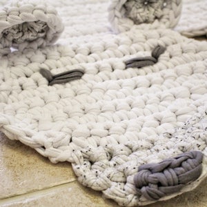 May include: A white crocheted rug shaped like an animal face with grey crocheted eyes and nose.