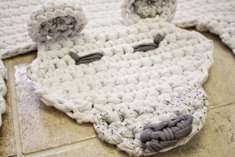 May include: A white crocheted rug shaped like an animal face with grey crocheted eyes and nose.