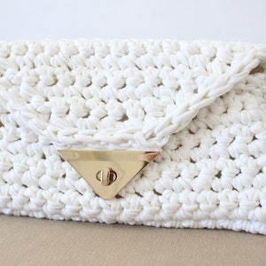 May include: A white crocheted clutch bag with a gold triangular clasp.