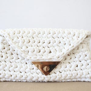 May include: A white crocheted clutch bag with a gold triangular clasp.
