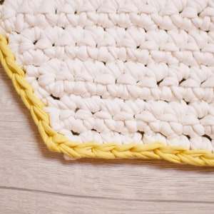 May include: A white crocheted rug with a yellow braided border.