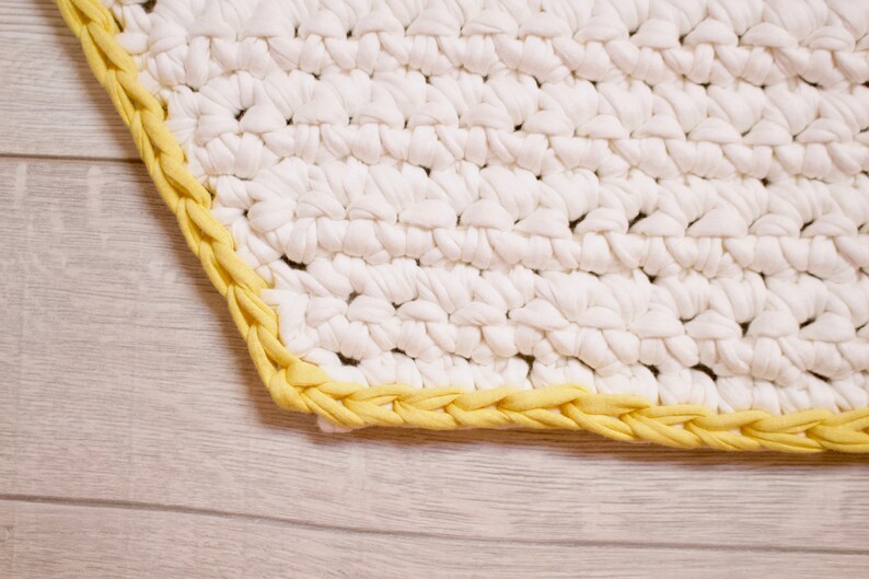 May include: A white crocheted rug with a yellow braided border.
