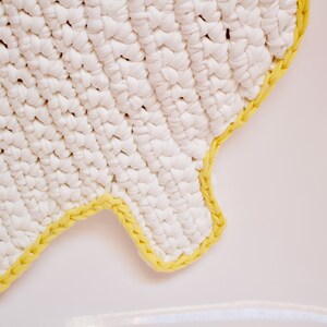 May include: White crocheted rug with a yellow crocheted border. The rug is shaped like a cloud.