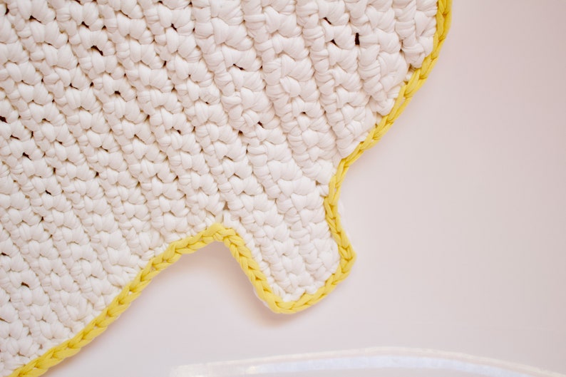 May include: White crocheted rug with a yellow crocheted border. The rug is shaped like a cloud.