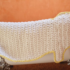May include: White crocheted bath mat with a yellow border. The mat is shaped like a foot and is placed in a white bathtub.