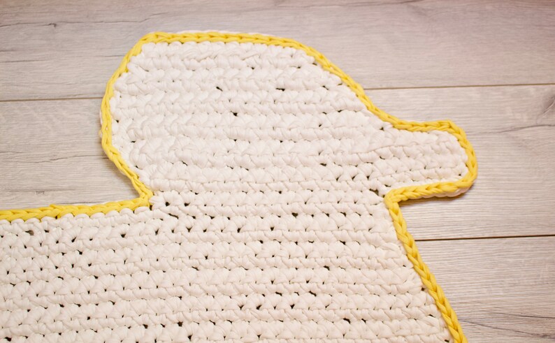 May include: White crocheted rug shaped like a duck with a yellow border.