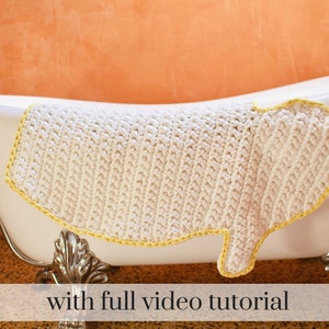 May include: A white crocheted bath mat with a yellow border. The mat is hanging over the edge of a white bathtub.