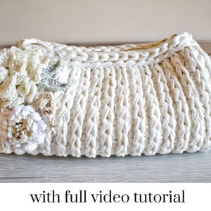 May include: White crocheted clutch bag with a zipper closure and a floral design. The bag is decorated with white and cream crocheted flowers.