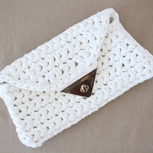 May include: A white crocheted clutch bag with a gold clasp.