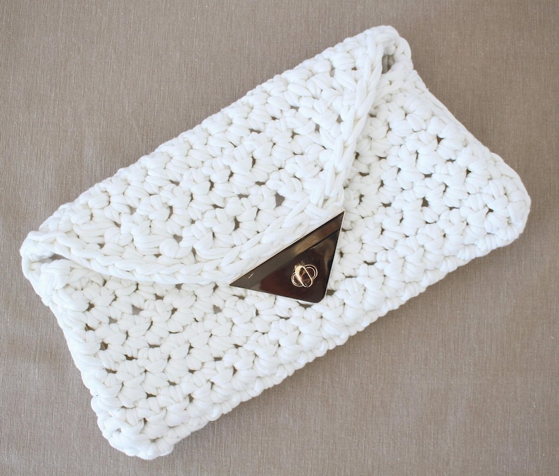 May include: A white crocheted clutch bag with a gold clasp.
