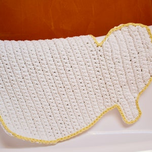 May include: White crocheted bath mat with a yellow border. The mat is shaped like a foot and has a textured surface.