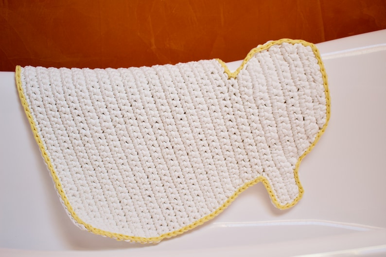 May include: White crocheted bath mat with a yellow border. The mat is shaped like a foot and has a textured surface.
