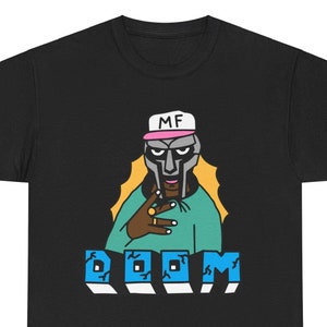 May include: Black t-shirt featuring a cartoon illustration of a rapper wearing a mask and a hat that says "MF DOOM". The text "DOOM" is written in blue and white letters below the rapper.
