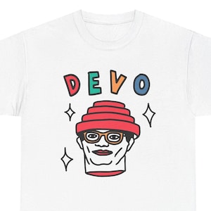 Op de afbeelding: Wit T-shirt met een kleurrijke illustratie van een persoon die een rode, meerlaagse hoed en een bril draagt. Het woord "DEVO" staat boven de illustratie.